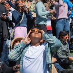 multitud observando un eclipse solar con gafas especiales bajo un cielo oscuro.