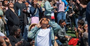 multitud observando un eclipse solar con gafas especiales bajo un cielo oscuro.
