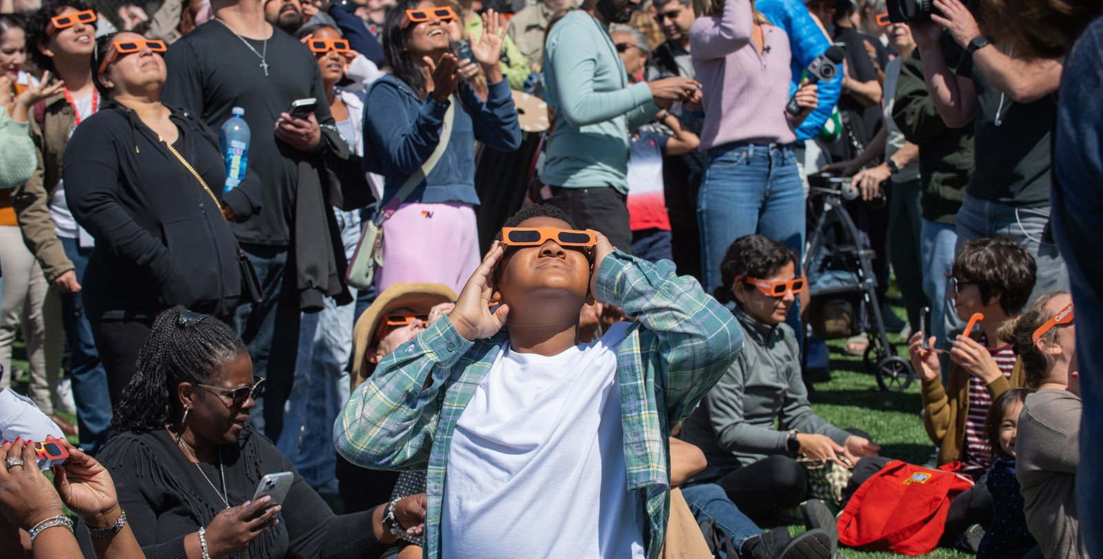 multitud observando un eclipse solar con gafas especiales bajo un cielo oscuro.