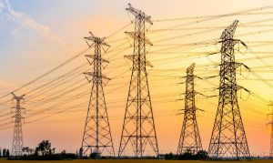 Torres de alta tensión eléctrica cruzando un campo seco bajo un cielo despejado durante un atardecer caluroso.